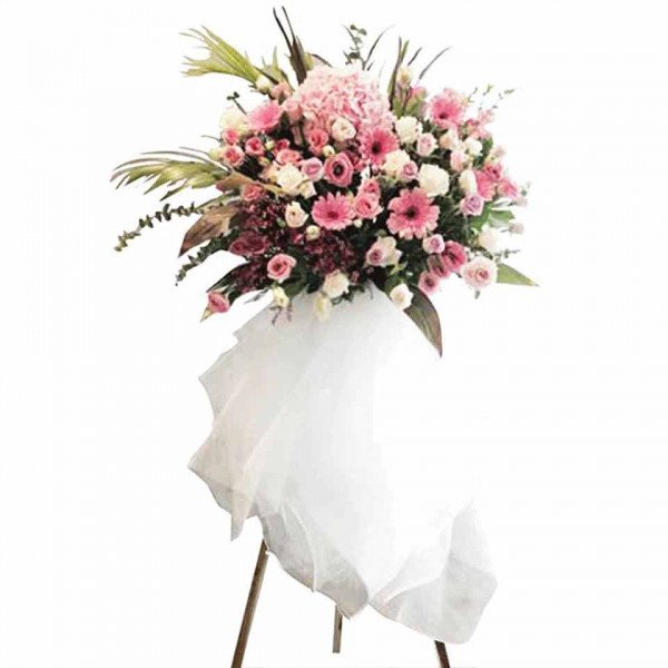 A tall, elegant floral arrangement with pink and white flowers on a stand, draped with white fabric.