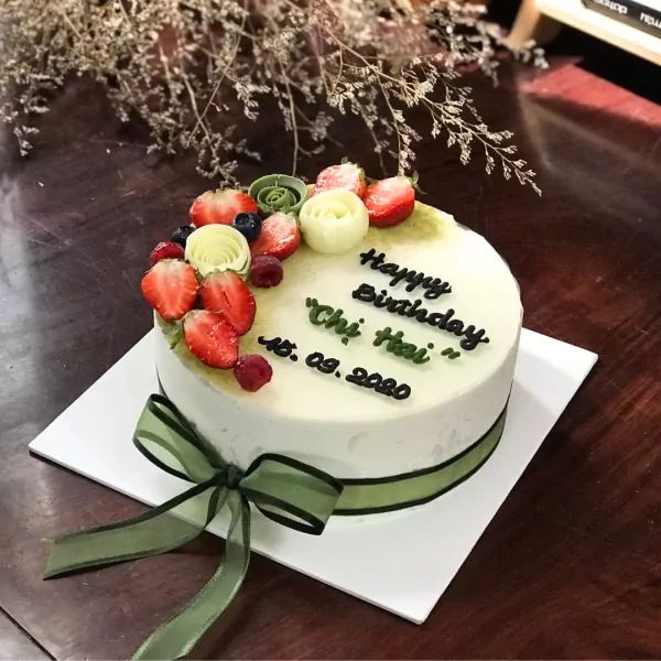 Round white cake with green ribbon, strawberries, blueberries, raspberries, and "Happy Birthday Chi Hai" message.