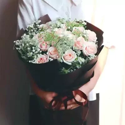 A bouquet of soft pink roses and baby's breath in brown paper.