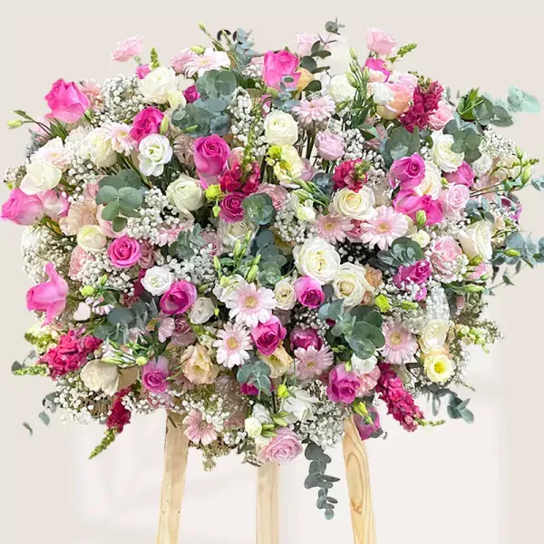 Large flower stand with pink and white roses, gerbera daisies, and filler flowers on a light background.