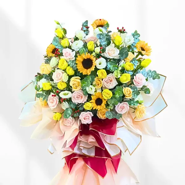 Large floral arrangement with sunflowers, roses, and greenery in a decorative stand.
