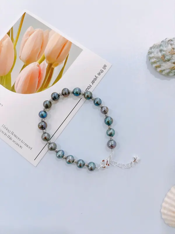 A dark blue pearl bracelet with silver accents and a clover charm.