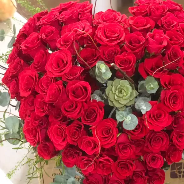 Heart-shaped arrangement of 99 red roses, succulents, and eucalyptus.