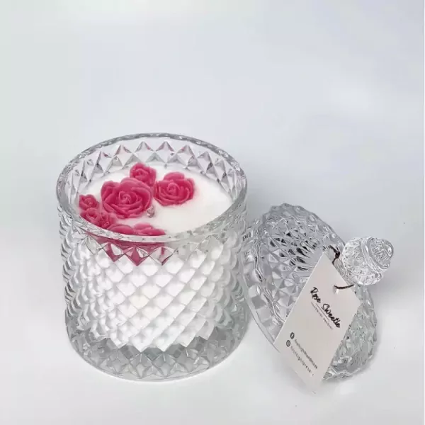 Scented candle in a clear glass jar with pink rose wax decorations and a detached lid.