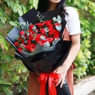 Woman holding a bouquet of 36 red roses wrapped in black paper and tied with a red ribbon.