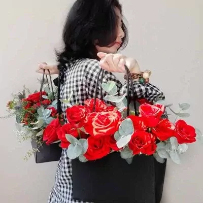 Woman carrying two black bags filled with red roses and greenery.
