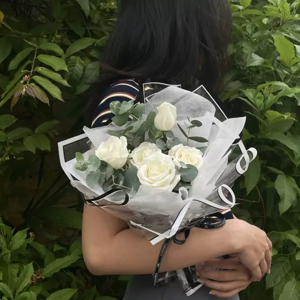 A bouquet of white roses with eucalyptus, wrapped in white paper and black ribbon.