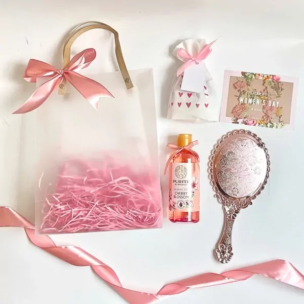 A gift set with a mirror, lotion, and a card, all wrapped in pink.