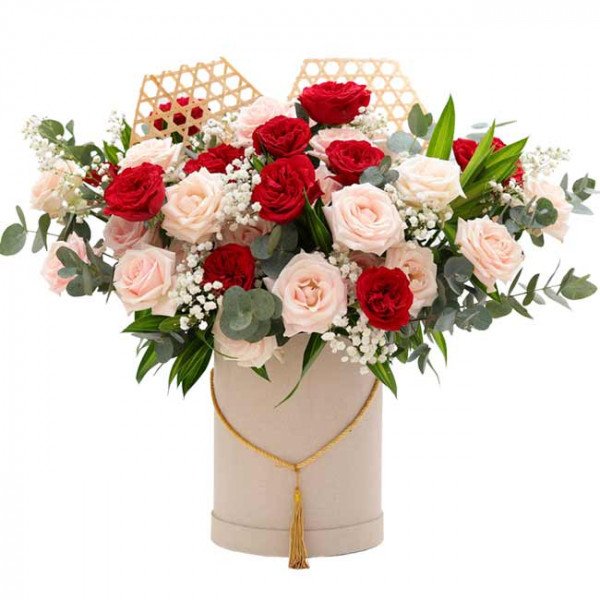 Round box of red and cream roses with decorative bamboo elements and gold tassel.
