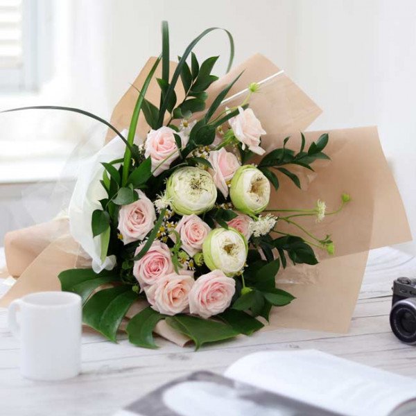 Bouquet of pink roses and white lotus flowers, with greenery, in light brown paper wrapping.