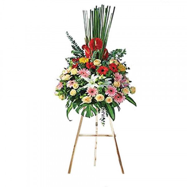 A large, vibrant flower arrangement with red, pink, yellow, and white flowers on a wooden easel.