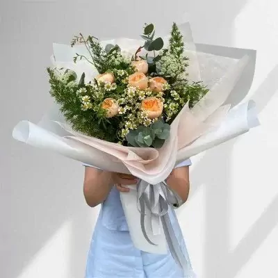 Bouquet of orange roses and greenery wrapped in white and pink paper with grey ribbon.