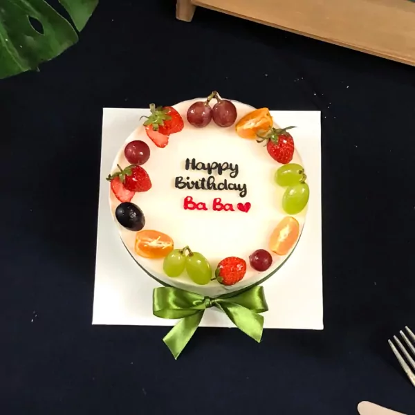 Fruit-adorned cake with "Happy Birthday Ba Ba" message and green bow.