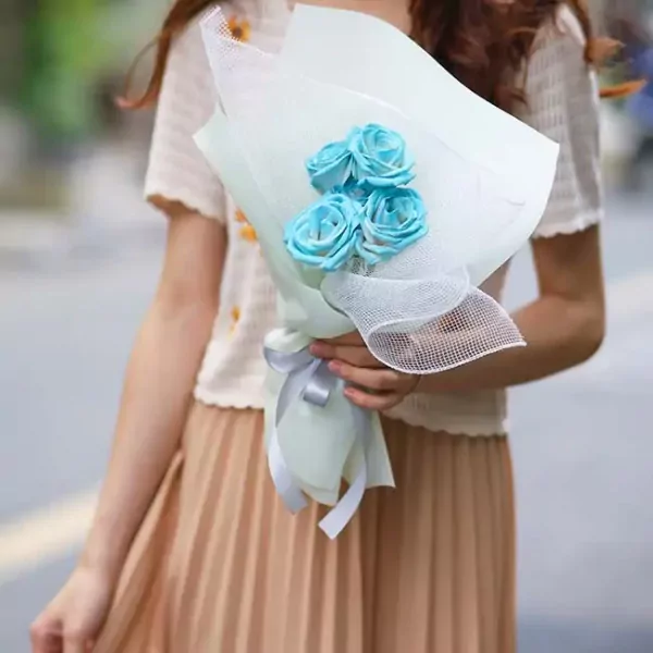 A bouquet of four bright blue roses, wrapped in light green and white paper, with a silver ribbon.