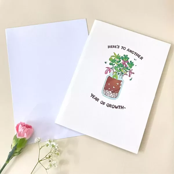 Card with plant illustration and "year of growth" text, next to white card and pink flower.