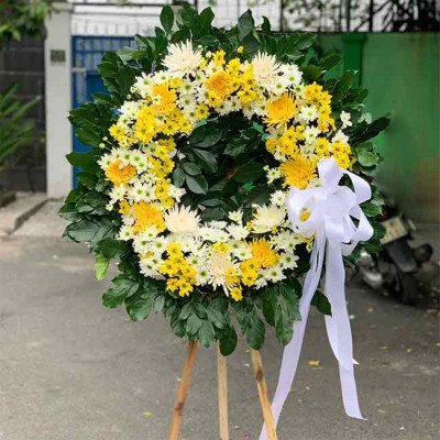 Funeral wreath with yellow and white chrysanthemums and a white ribbon on a stand.