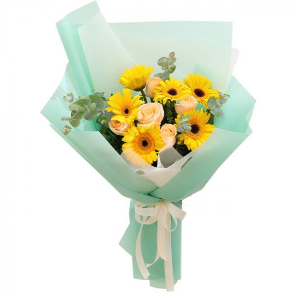 A bouquet of yellow gerbera daisies and light peach roses wrapped in mint green paper.