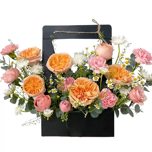 A floral arrangement in a black basket with peach roses, pink carnations, and daisies.