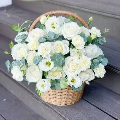 Basket of white roses, carnations, and lisianthus with eucalyptus.