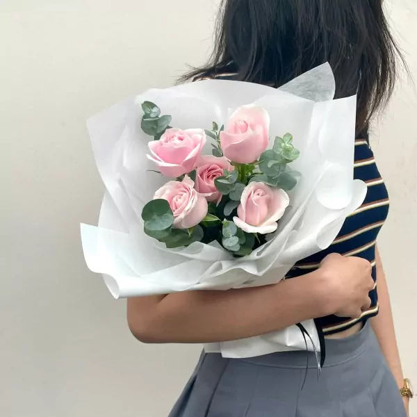 A bouquet of pink roses and eucalyptus leaves wrapped in white paper.