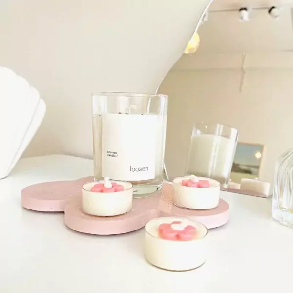 Flower-shaped tealights and a jar candle on a pink tray.