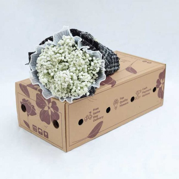 Bouquet of white baby's breath flowers in a black and white tweed wrap, resting on a brown cardboard box.