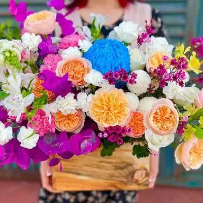 A pastel purple and blue flower box with roses, carnations, and chrysanthemums.