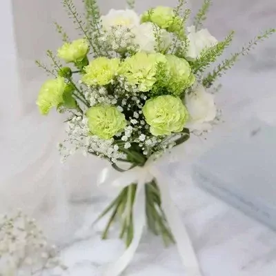 Bridal bouquet with green carnations, white roses, and baby's breath tied with a white ribbon.