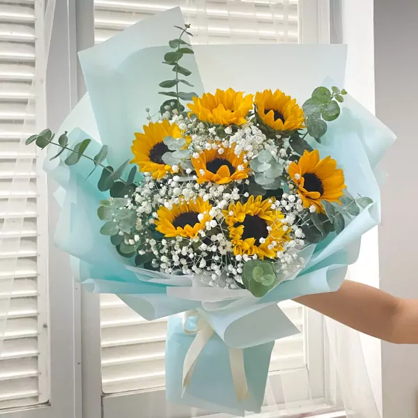 A bouquet of sunflowers and baby's breath wrapped in light blue paper.