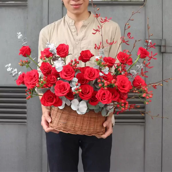 Man holding a basket of red roses, eucalyptus, and red berries.