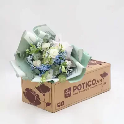 Bouquet of white roses, blue hydrangeas, and baby's breath in green paper on a brown box.