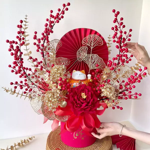 Lucky cat in a red flower box with gold accents and red berries, a symbol of prosperity.