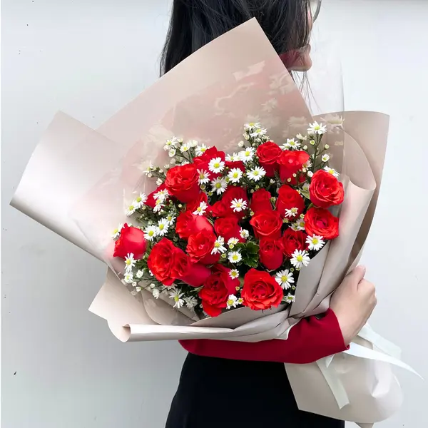 Bouquet of red roses and white daisies in elegant wrapping.