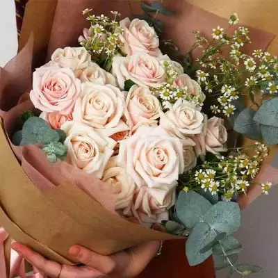 Bouquet of pale pink roses and daisies, wrapped in brown paper.