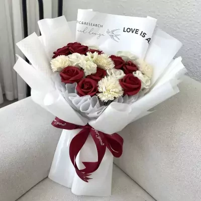 Red and white flowers in a bouquet wrapped in white paper, tied with a dark red ribbon.