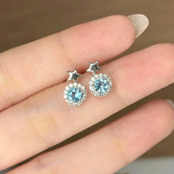 Starlight blue topaz stud earrings with star detail, surrounded by small clear stones.