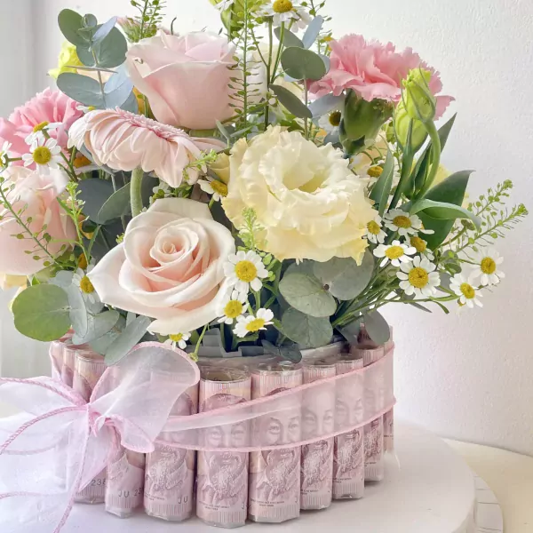 Money cake adorned with pink and cream roses, daisies, and greenery.