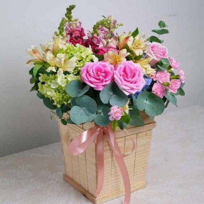 Wooden box arrangement of pink roses, hydrangea, carnations, snapdragons and eucalyptus.
