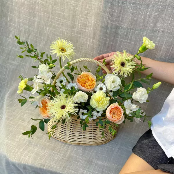 Basket of yellow and orange roses, carnations, and daisies with greenery.