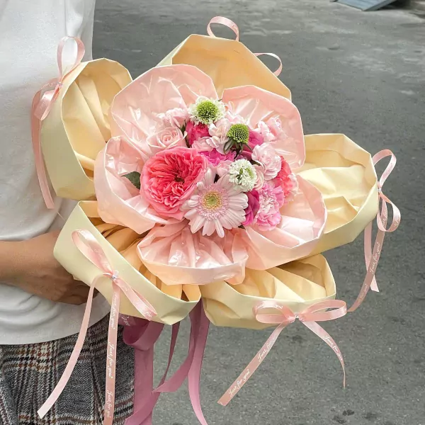 Pink and cream floral arrangement in a petal-shaped box with ribbon accents.