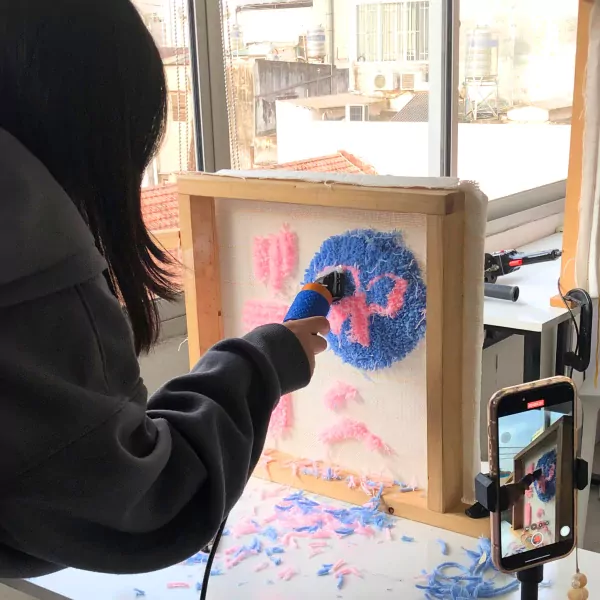 Person using a punch needle tool on a fabric frame with blue and pink yarn, creating a circular design.