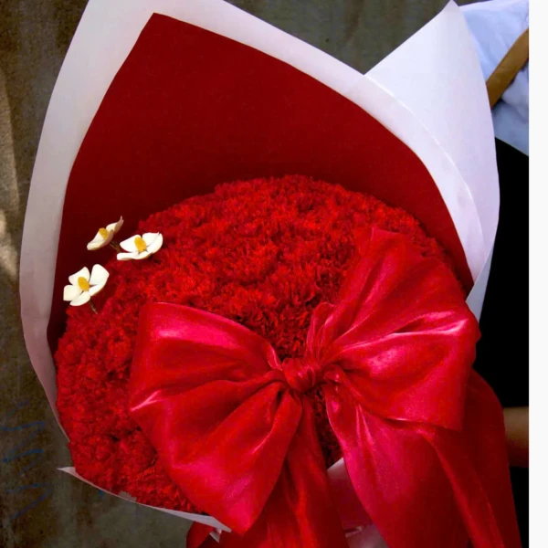 A bouquet of red carnations and wooden daisies, tied with a red ribbon.