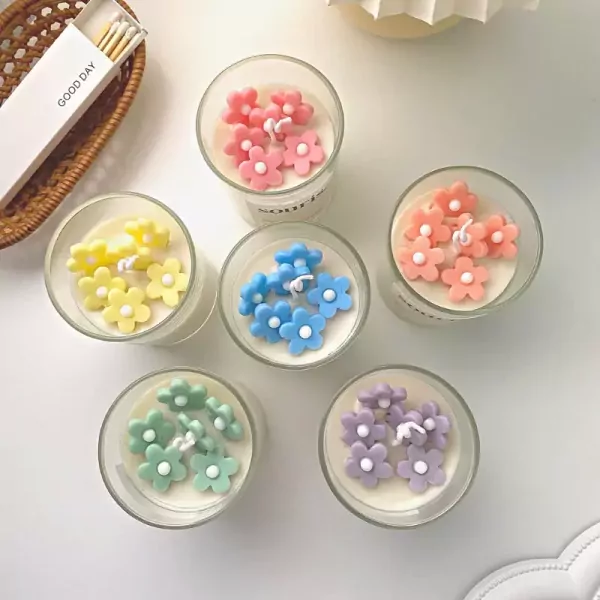 Small glass candles in a gift box, each topped with colorful flower-shaped wax decorations in pink, yellow, blue, peach, mint, and purple.
