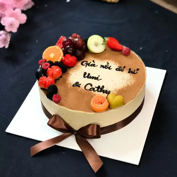 Tiramisu cake decorated with fresh fruit and a brown ribbon.