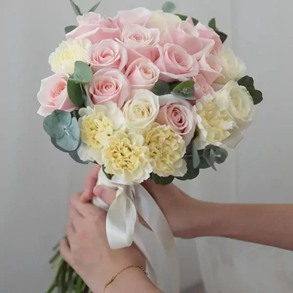 A bridal bouquet of pink and white roses and yellow carnations, tied with a white ribbon.