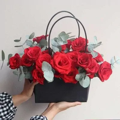 A black bag full of red roses and eucalyptus.