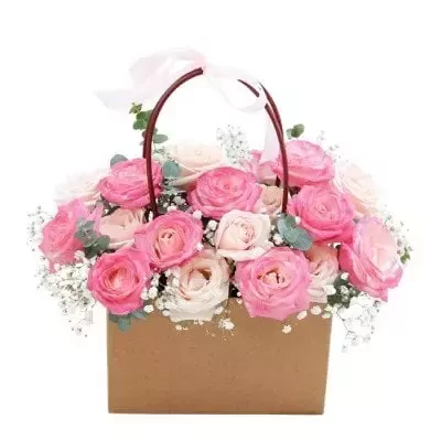 Basket of pink and cream roses with baby's breath and greenery, tied with a pink ribbon.