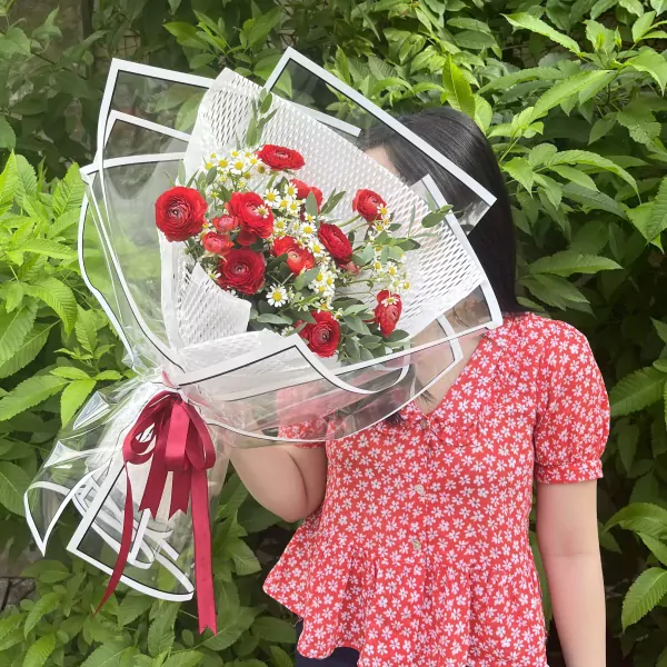 Woman in red floral top holding a bouquet of red ranunculus and white tana flowers.
