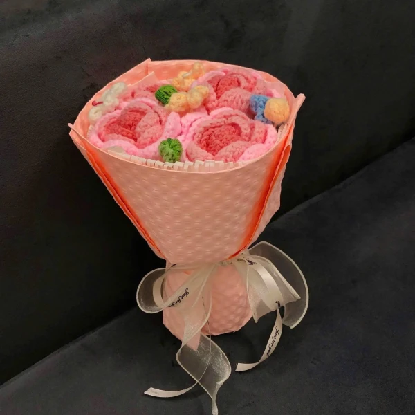 Knitted pink rose bouquet with colorful accents and a ribbon bow, wrapped in pink paper.
