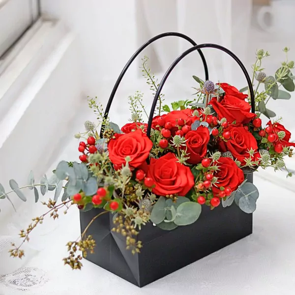 Black bag arrangement with red roses, berries, thistle, and greenery.